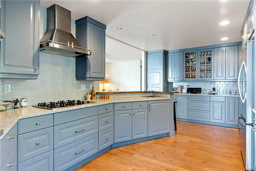 Kitchen with blue cabinets, granite counters, stainless steel appliances, and wood floor