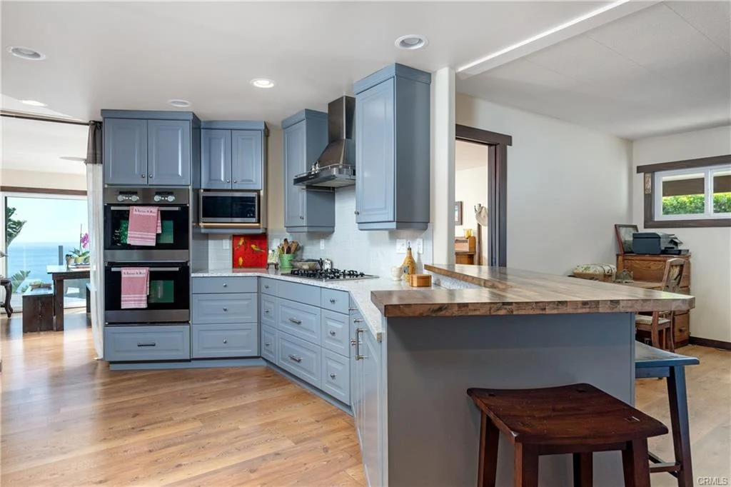 Kitchen with blue cabinets, gas stove, range hood, and oven below