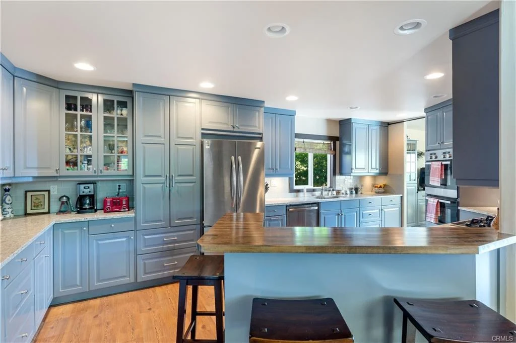 Kitchen with light blue cabinets, stainless steel appliances, wooden floor, and bar stools