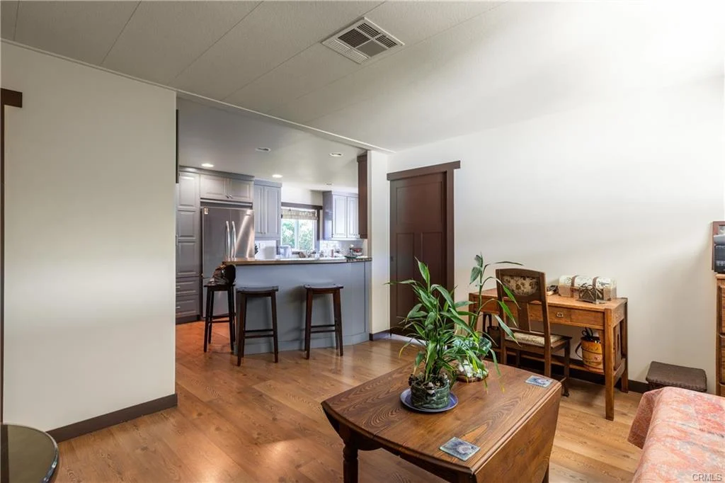 Living room with wooden floor, small plant, and kitchen with bar seating