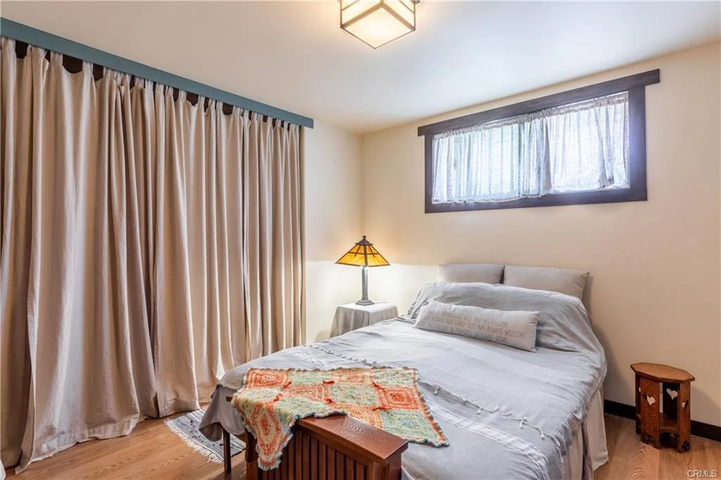 Bedroom with bed, bedside table, lamp, curtains, and wooden floor
