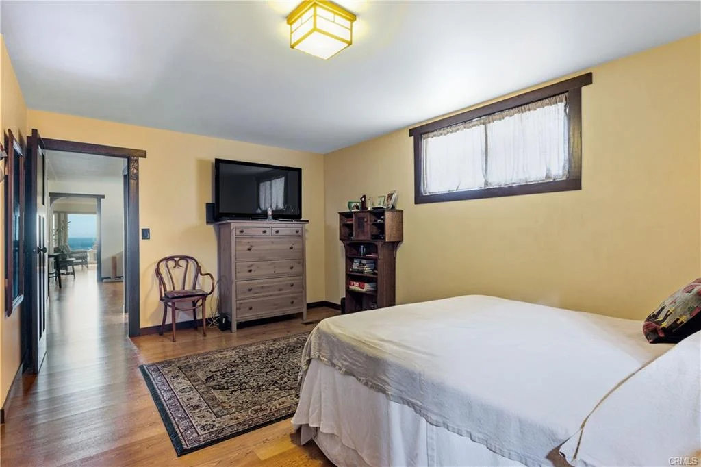 Bedroom with bed, dresser, TV, chair, and window with light yellow walls