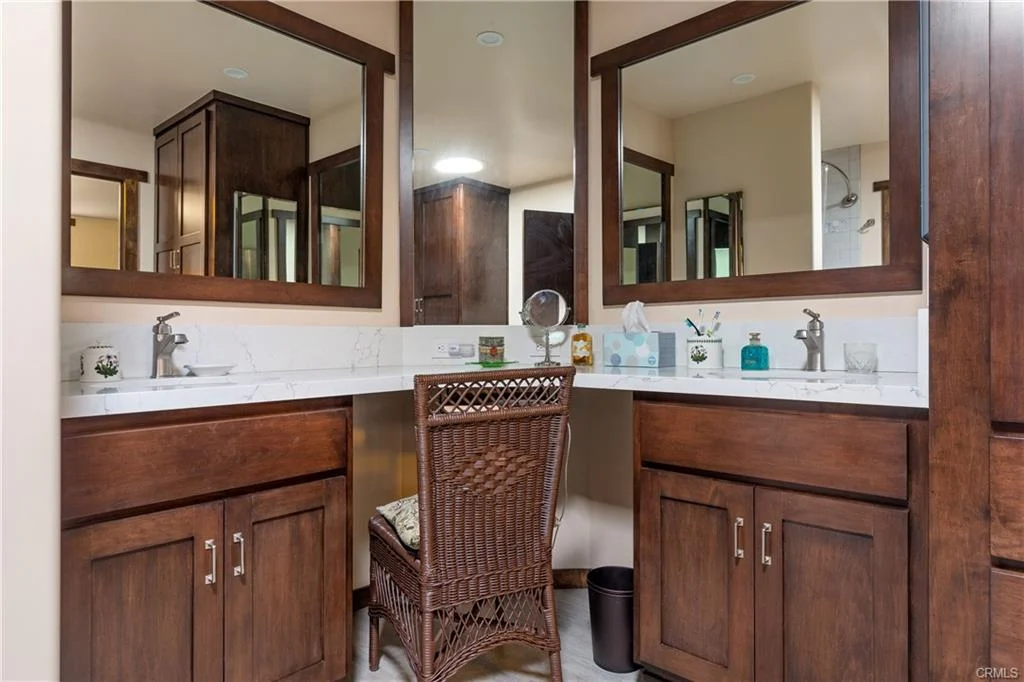 Bathroom with double sink, mirrors, wooden cabinets, and chair