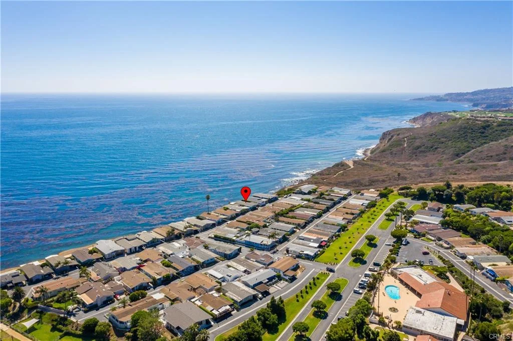 Aerial view of houses with road, trees, and ocean with map marker