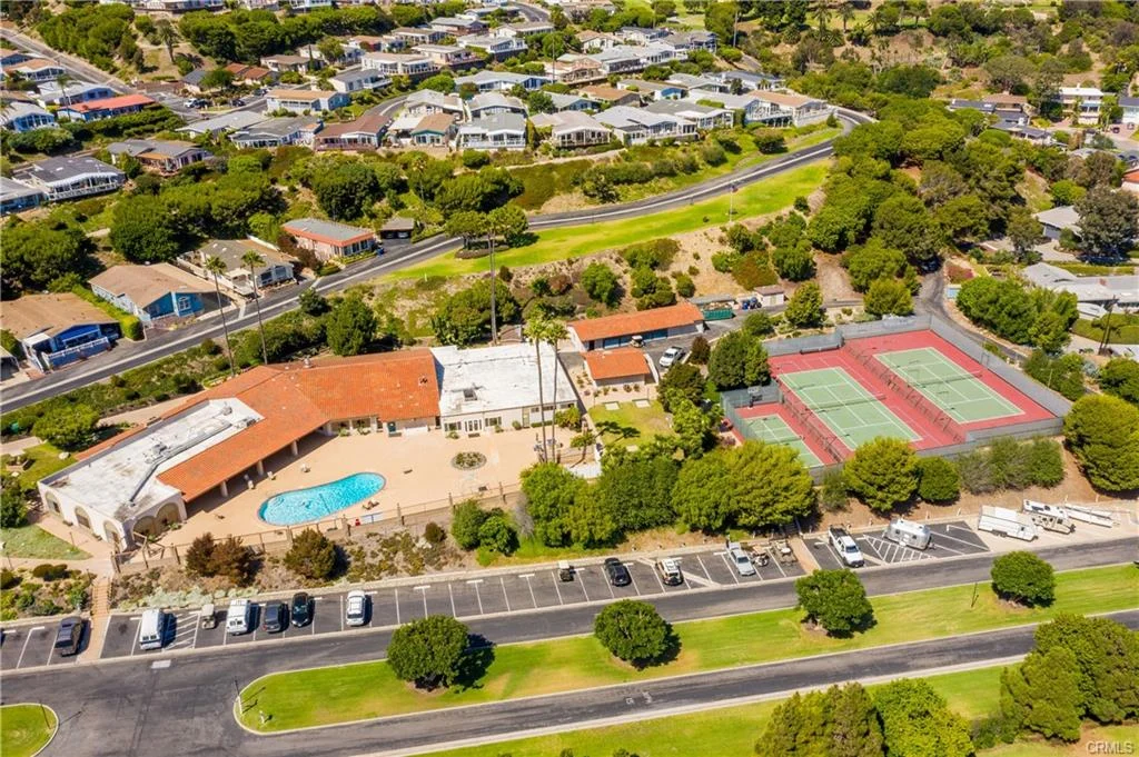 Aerial view of facility with pool, tennis courts, and nearby houses with greenery