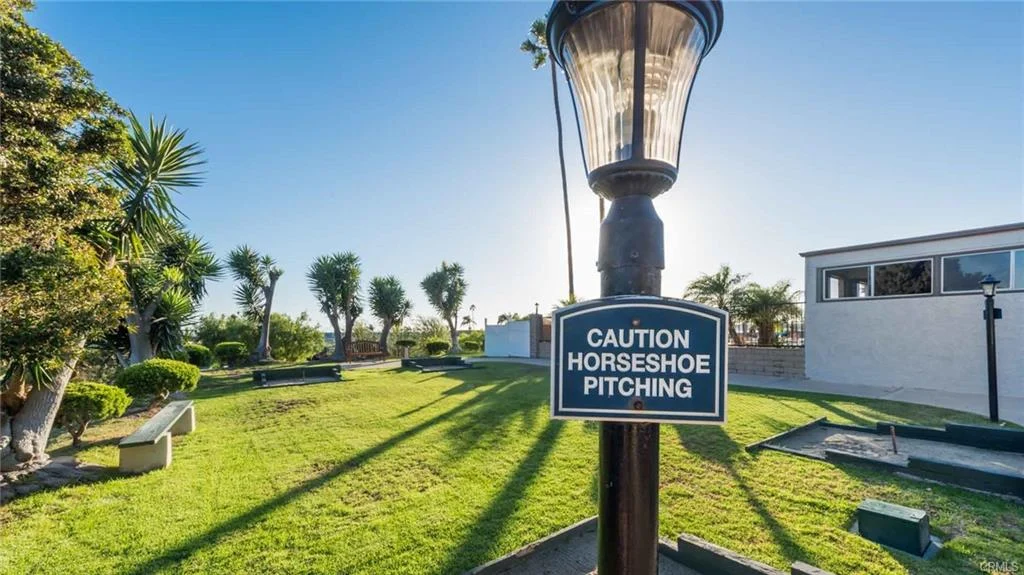Lamp post with caution sign, grass, palm trees, and buildings