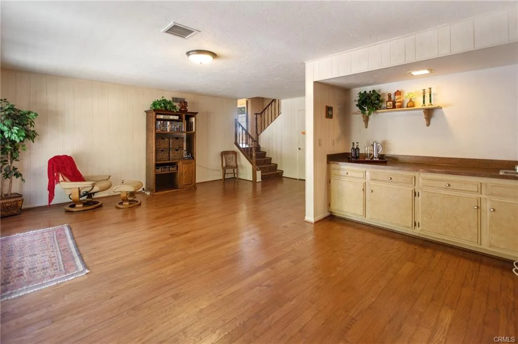 Interior room with hardwood floors, bar area, staircase, and plant.