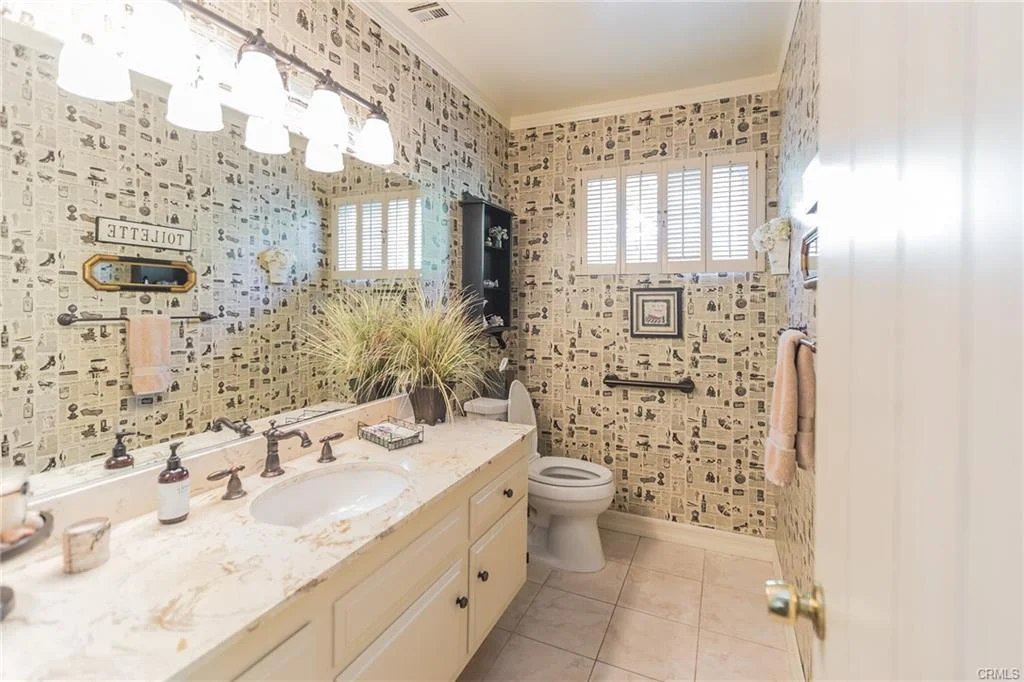 Bathroom with double sink, wallpaper, windows, and plants.
