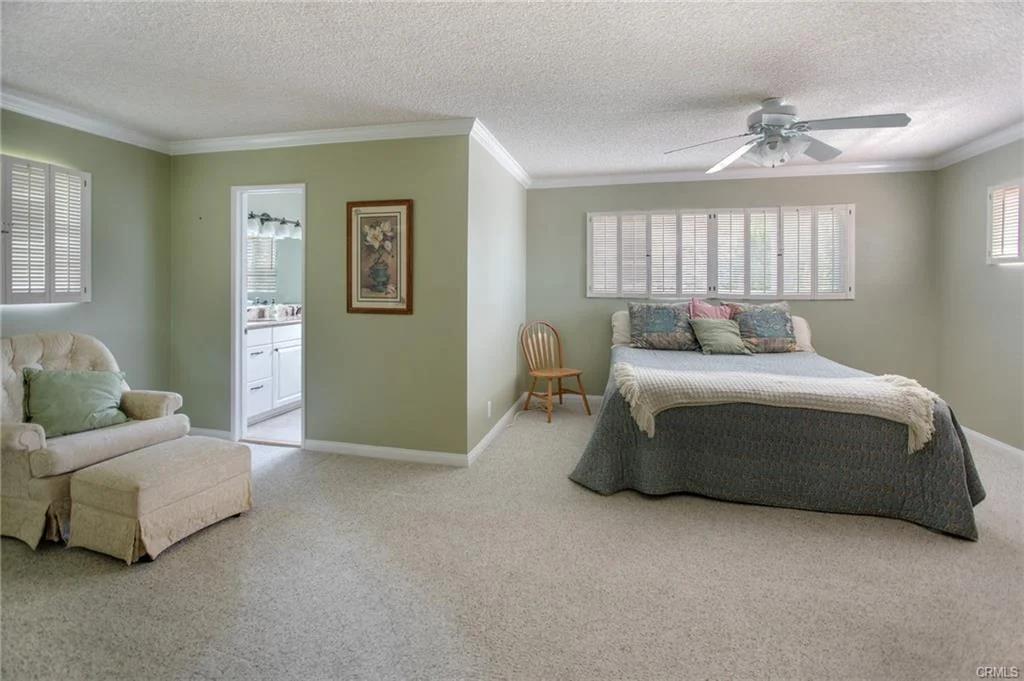 Bedroom with bed, ceiling fan, window, armchair, and carpet.