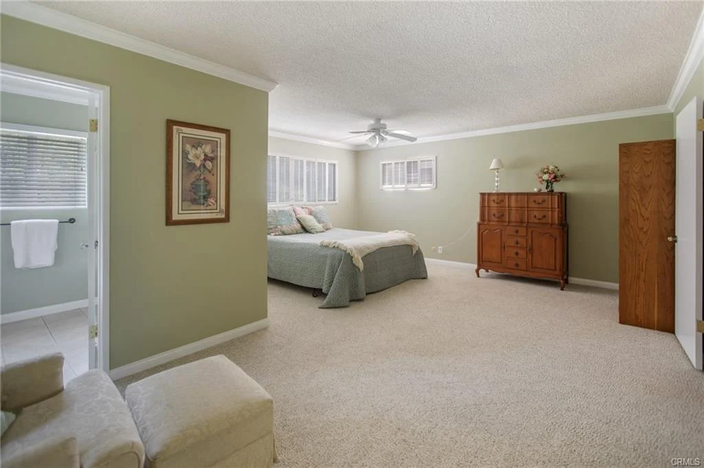 Bedroom with large bed, dresser, ottoman, and windows.