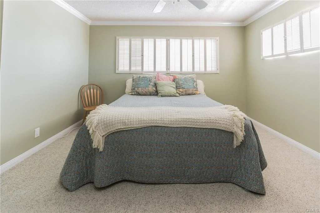 Bedroom with bed, decorative pillows, wooden chair, and windows.