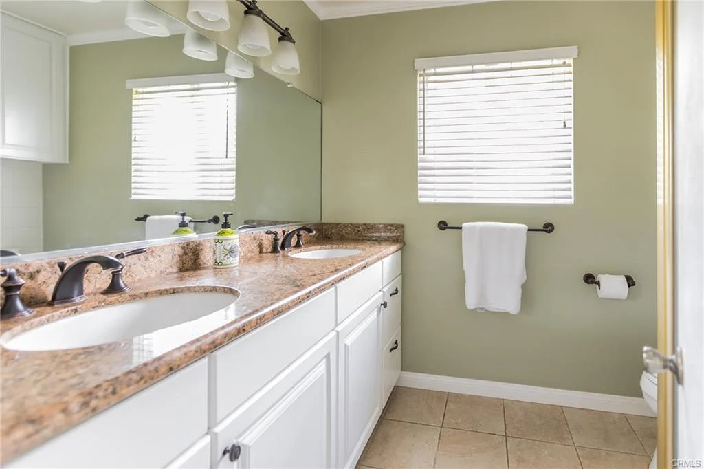 Bathroom with double sinks, granite countertop, mirror, and window.