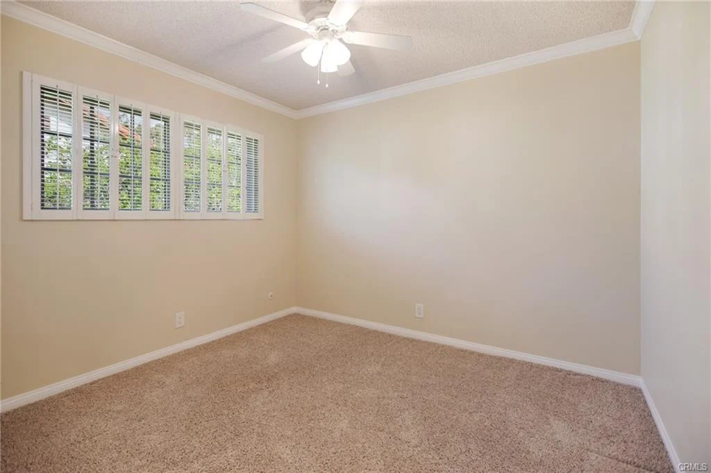 Room with beige walls, carpet, ceiling fan, and windows.
