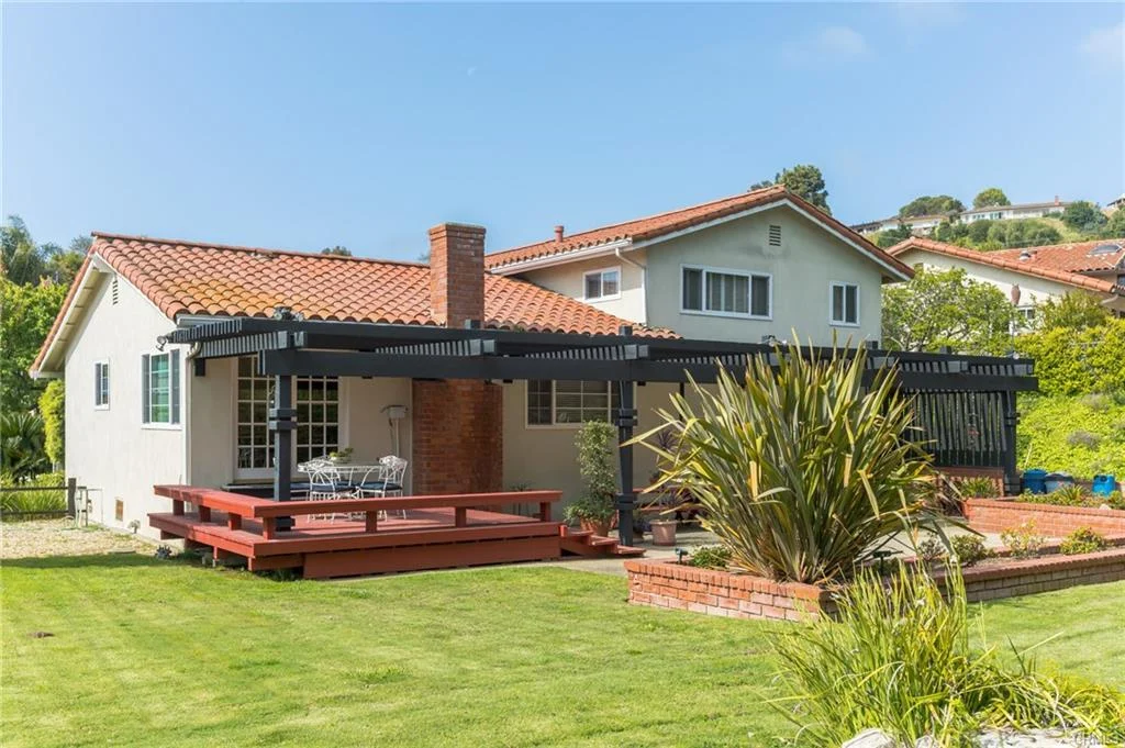 Backyard with wooden deck, seating, plants, and house, California real estate.