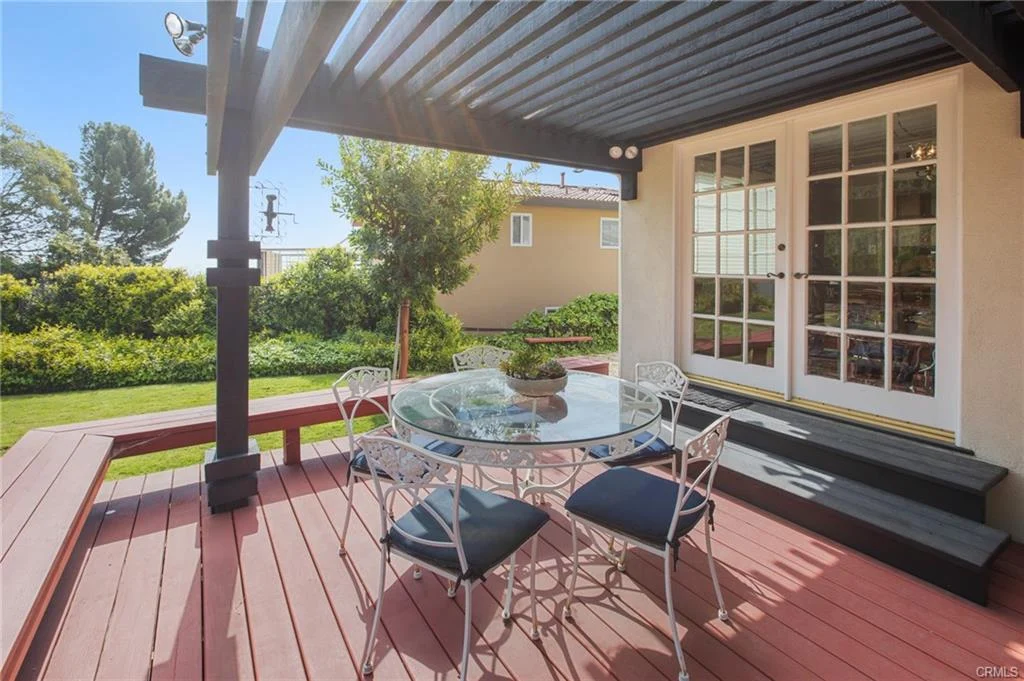 Patio with glass table, chairs, plants, and house, California real estate.