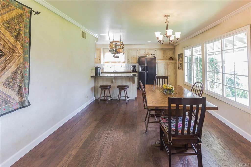 Dining area with wooden table, chairs, kitchen bar, and large windows