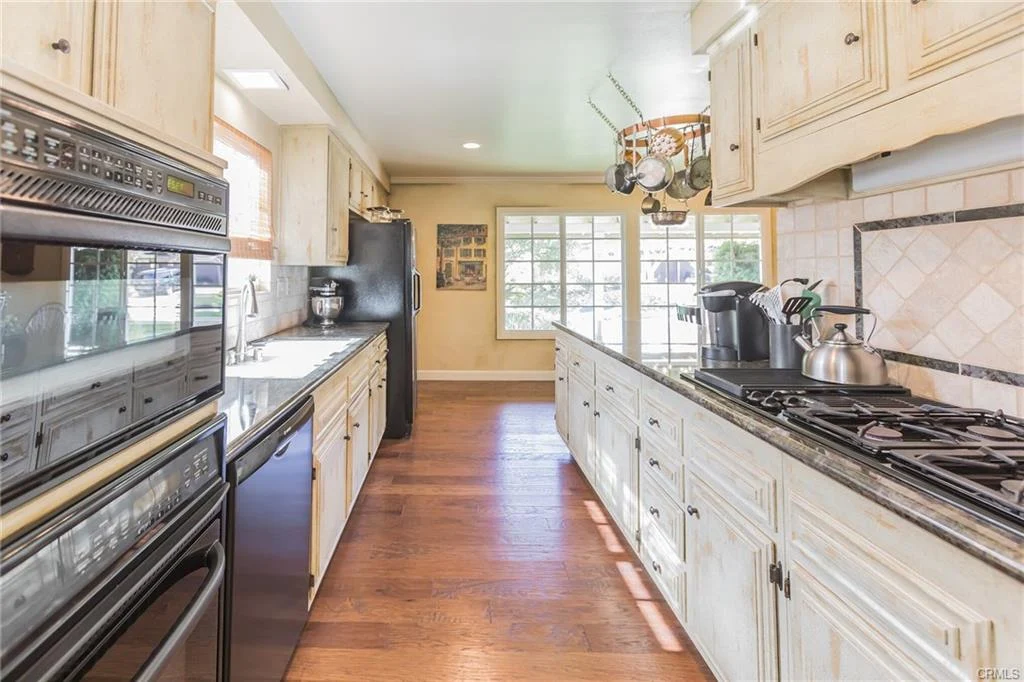 Kitchen with wooden cabinets, long countertop, appliances, and large windows