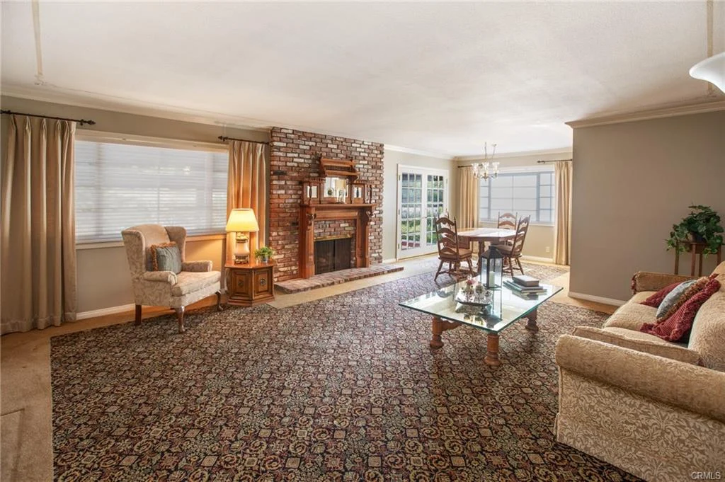 Living room with brick fireplace, glass coffee table, dining area, and large windows