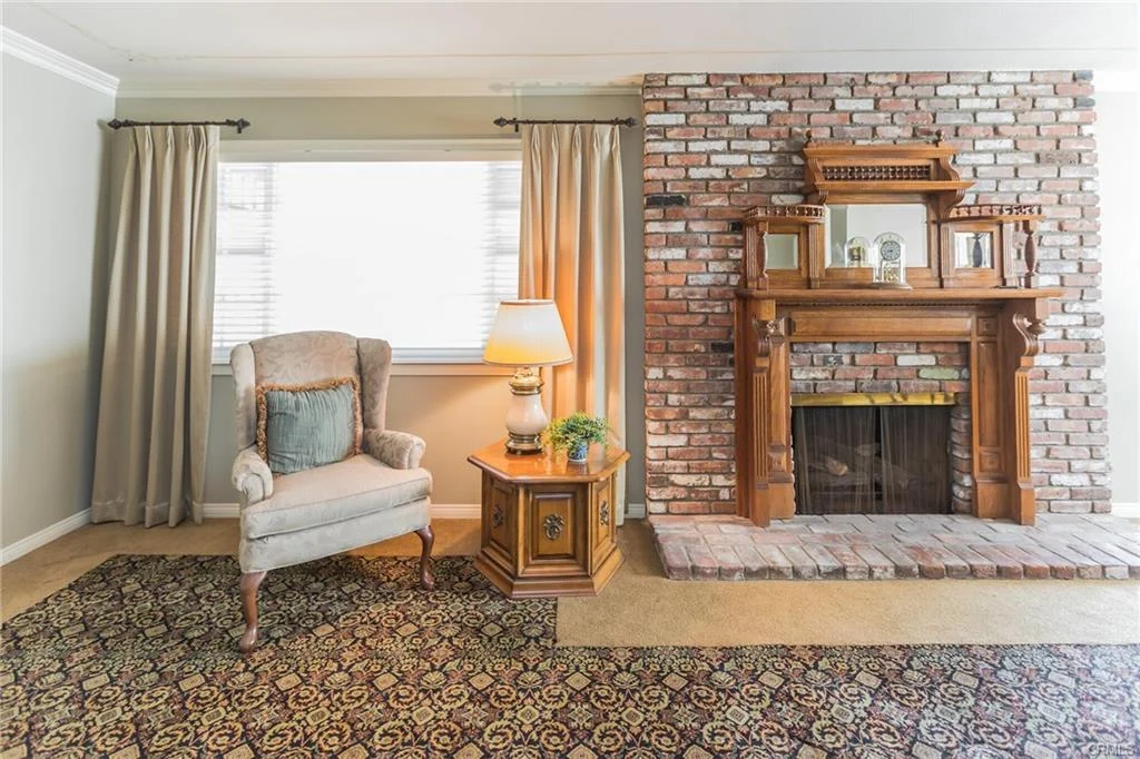 Living room with brick fireplace, wooden mantel, armchair, side table, and plant