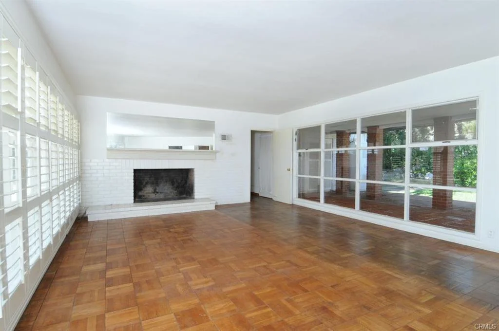 Empty room with wood floor, large windows with shutters, fireplace, and glass sliding door to outside.