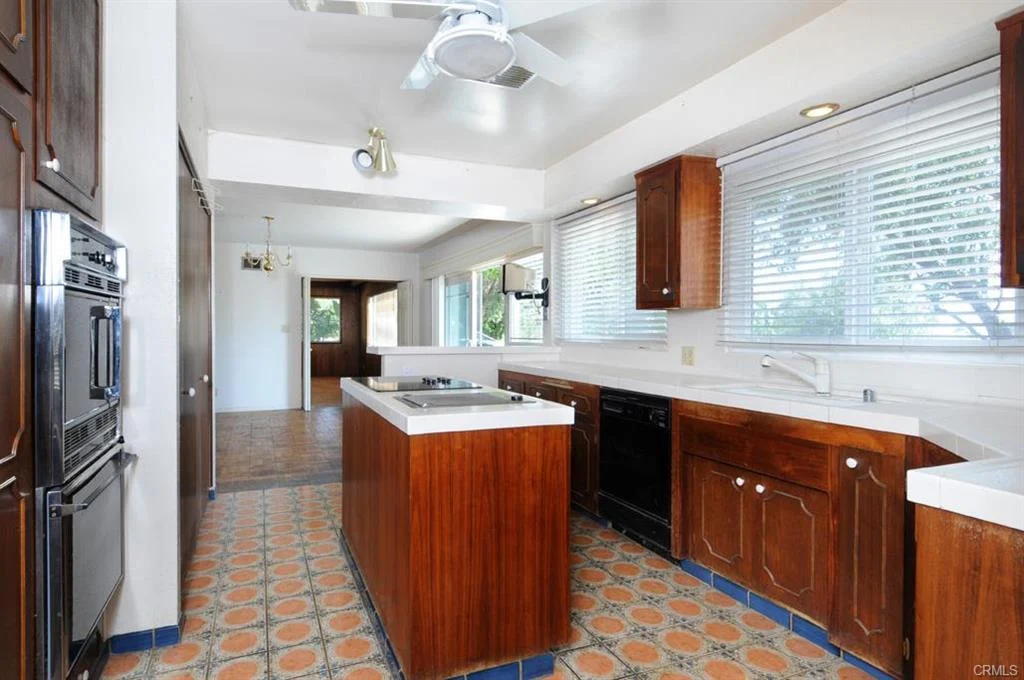 kitchen with wooden cabinets, island with cooktop, large windows, and patterned tile floor.