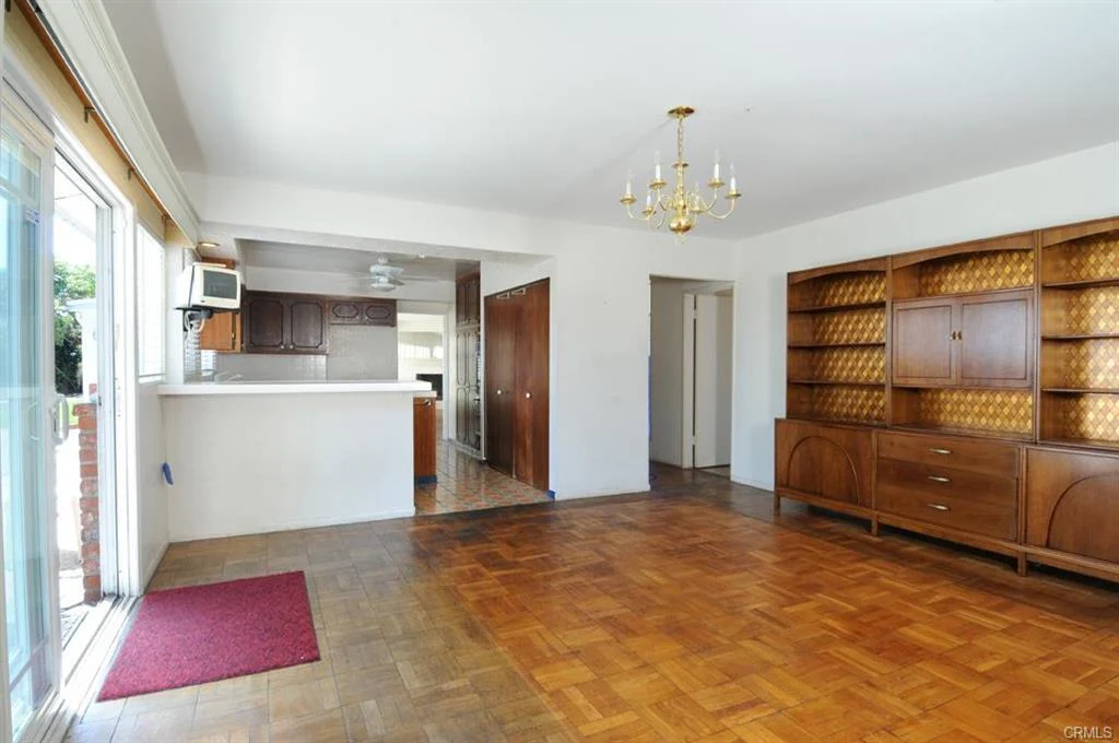 Empty room with wooden floor, chandelier, wooden cabinet, window, and door to outside.