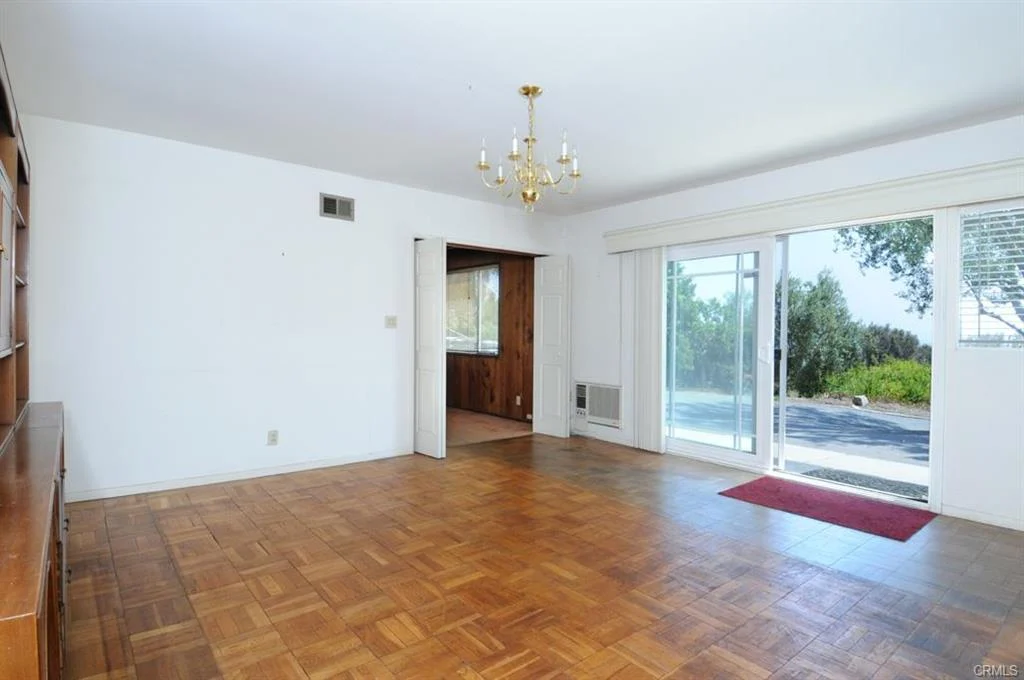 Empty room with wooden floor, a chandelier, and glass sliding doors to outside.
