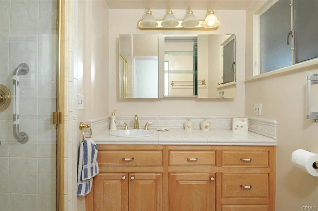 Bathroom with double sink, cabinets, mirror, shower, lights, and towel