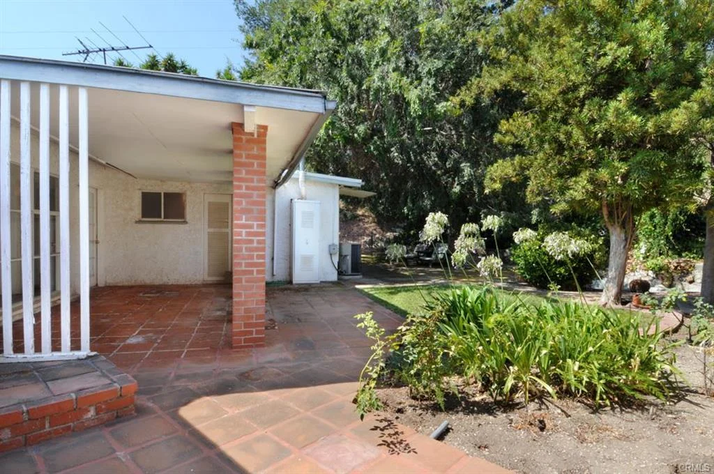 Backyard with patio, tile floor, plants, trees, walls, and small structure