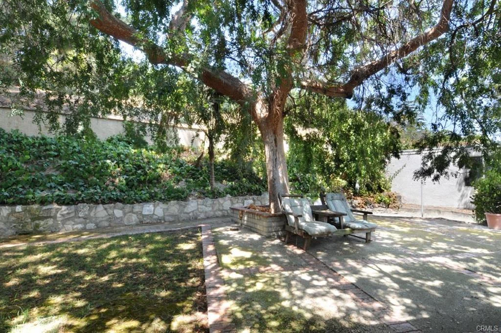 Patio with chairs, tree, stone wall, and greenery