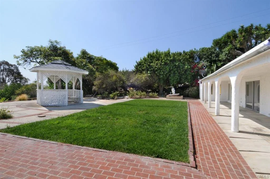 Outdoor area with gazebo, green plants, lawn, and building with white columns.