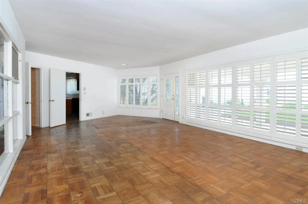 Empty living room with wood floor, white walls, and large windows with shutters.
