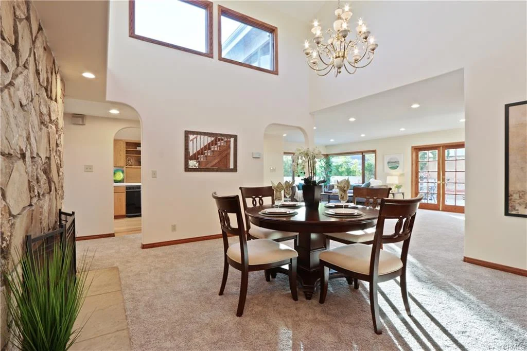 Dining area with round table, chairs, windows, and chandelier.