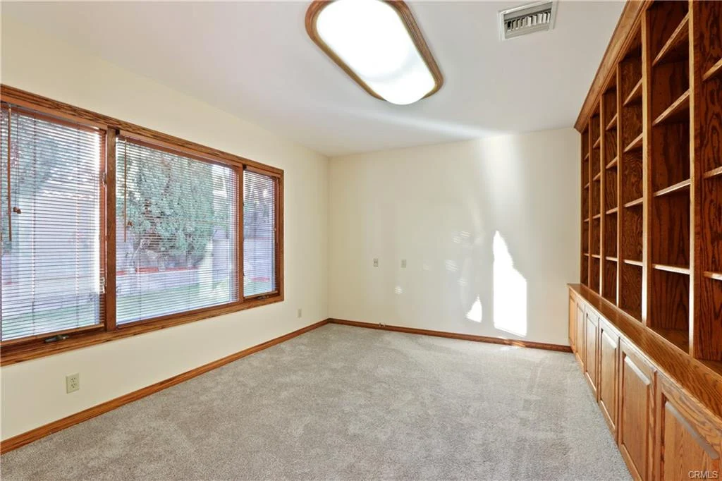 Room with beige walls, carpet, windows, and built-in bookshelf.