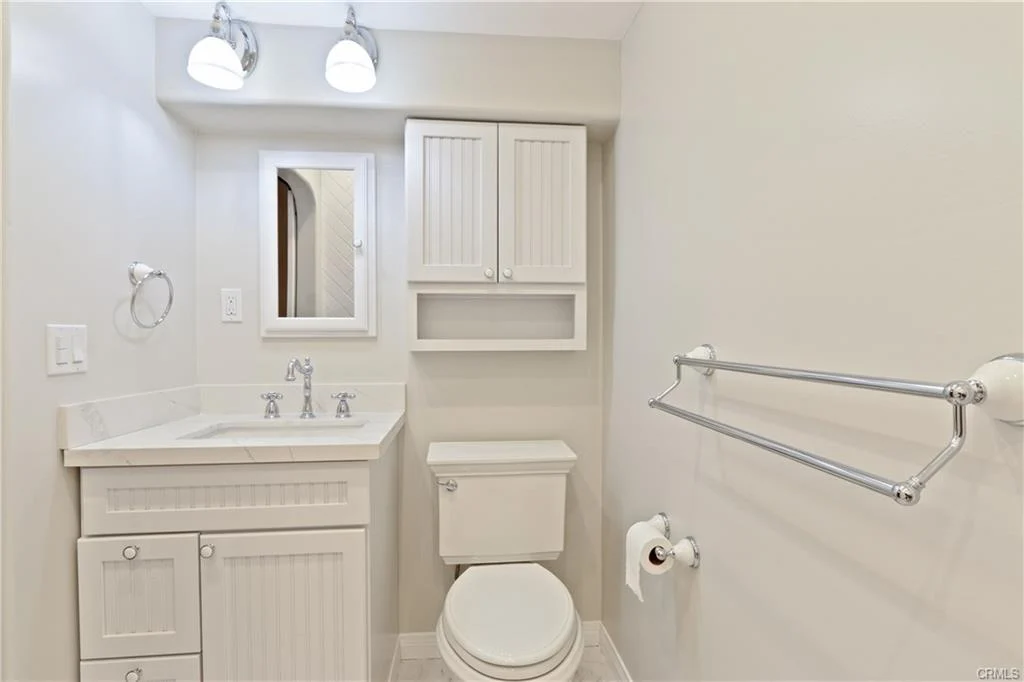 Bathroom with white cabinets, sink, mirror, and toilet.