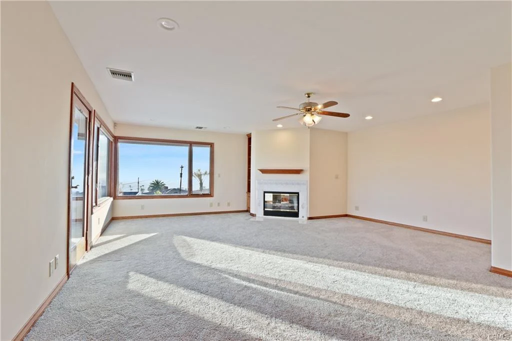 Living room with carpet, ceiling fan, large windows, and fireplace.