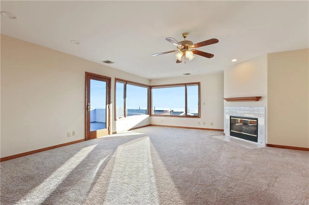 Living room with large windows, ceiling fan, and fireplace.