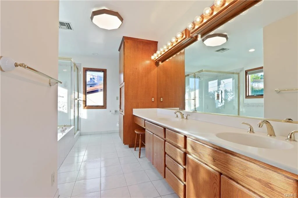Bathroom with double sinks, wooden cabinets, mirror, and windows.