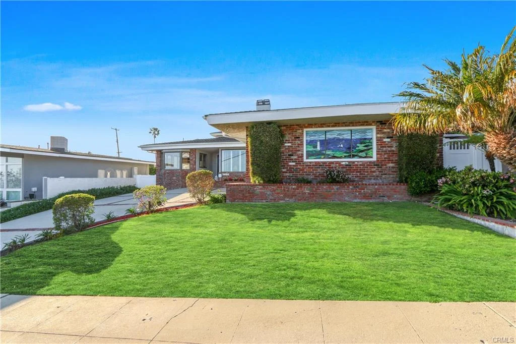 Lawn in front of a house with large window, plants, and palm trees, California real estate.
