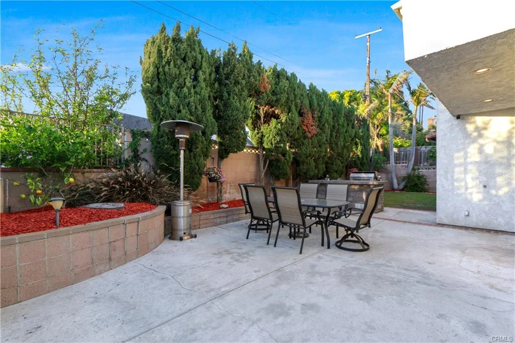 Backyard patio with dining table, chairs, and plants, California real estate house.