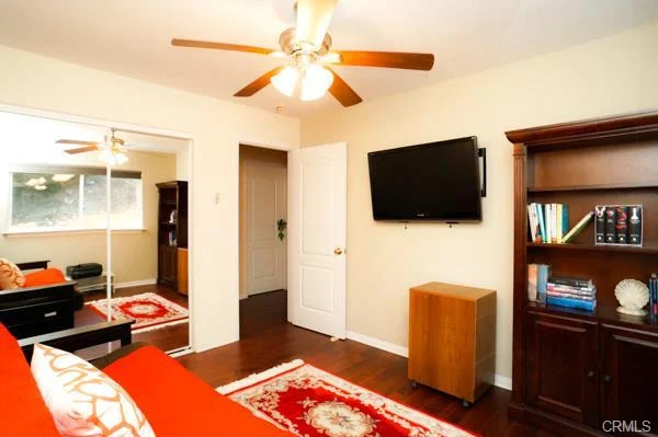 Room with a ceiling fan, a wall-mounted TV, a bookshelf, and a red rug.