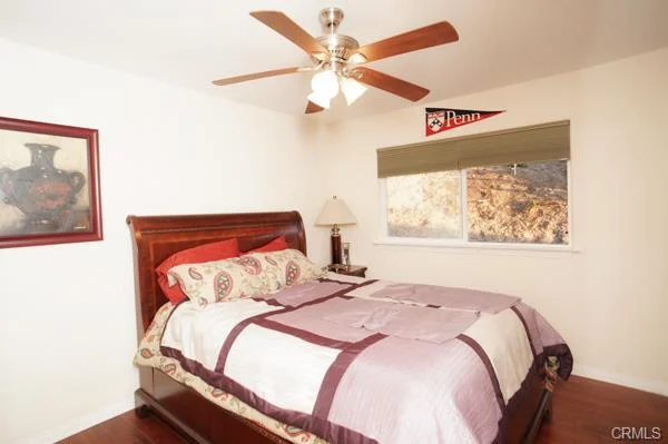 Bedroom with a wooden bed, a patterned blanket, a ceiling fan, and a window with blinds.