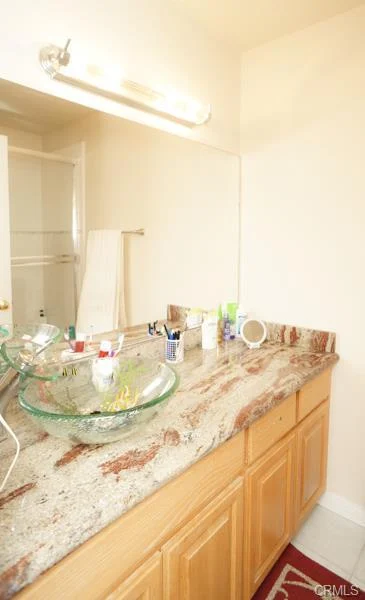 Bathroom with a sink, a stone countertop, light wood cabinets, and a rug.