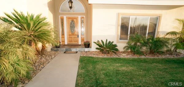 California real estate house, a wooden door, large windows, green grass, and palm plants.