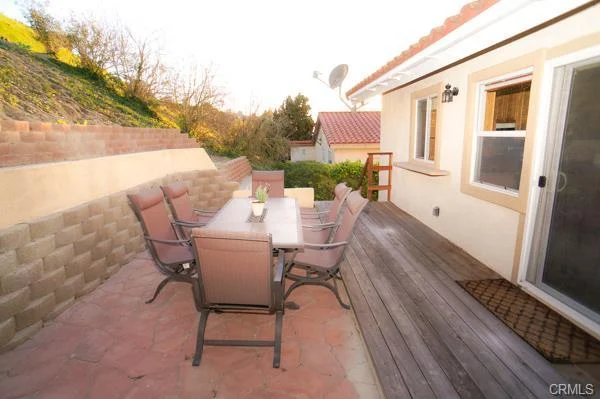 a patio with a table, chairs, a wall, and plants.