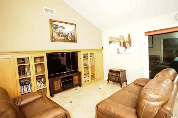 A living room with two brown leather sofas, a TV cabinet, built-in shelves, a framed picture, and a window.