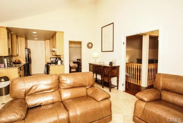 A living room with two brown leather couches, a dining area, a kitchen, and artwork.