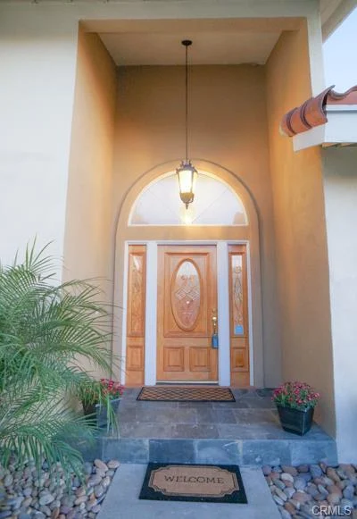 California real estate house, a wooden door with glass, palm plants, stone steps, and a welcome mat.