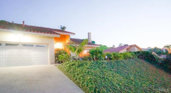 California real estate house, a garage, a driveway, and a hill with plants.