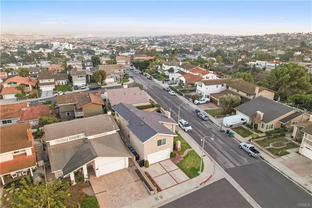 Aerial view of a suburban neighborhood featuring various houses, trees, and a street lined with parked cars.